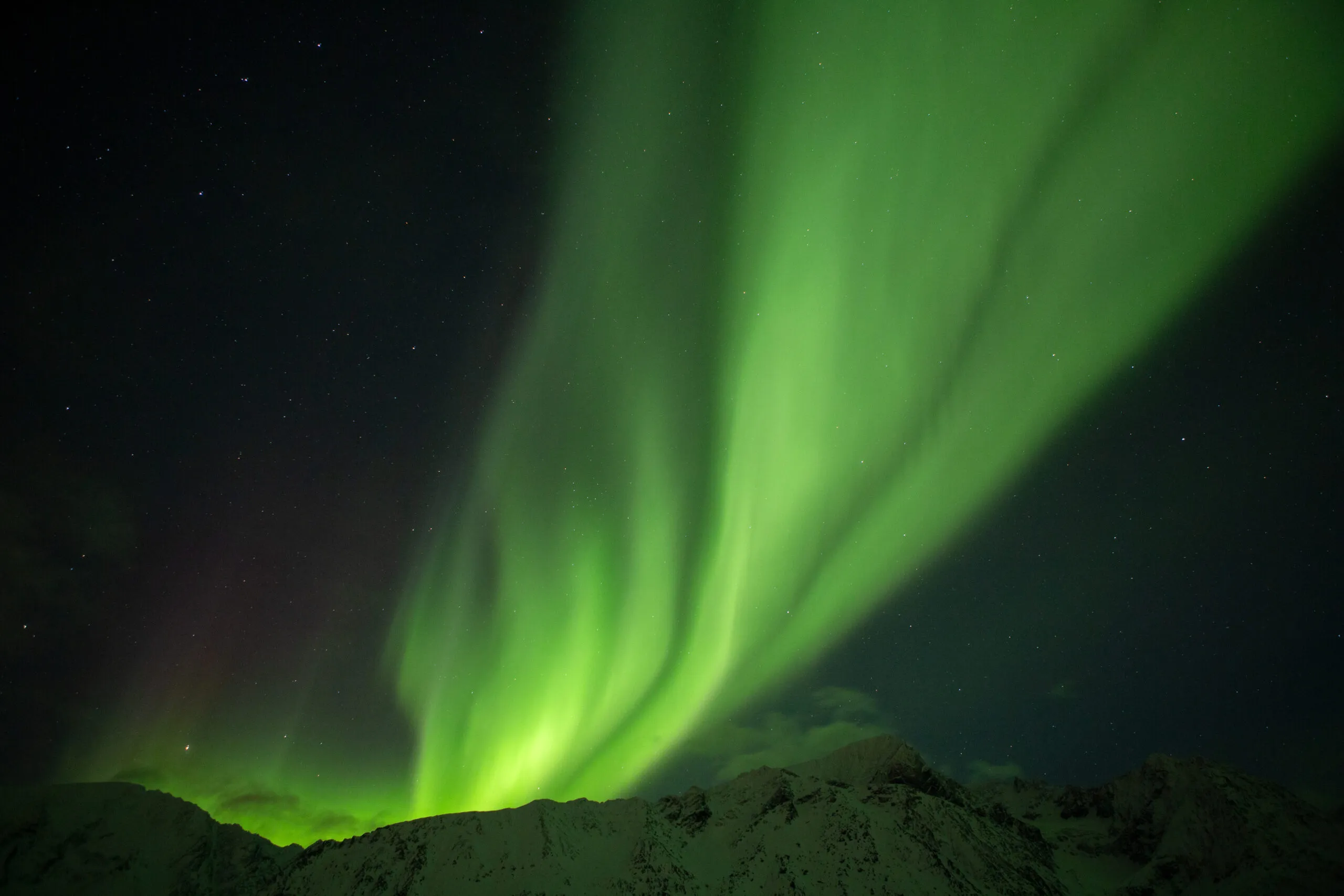 Ein starkes Nordlicht erscheint hinter einem Berg in Norwegen.