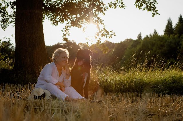 Schwarzer Hund und Besitzerin sitzen an einem sonnigen Tag unterm Baum