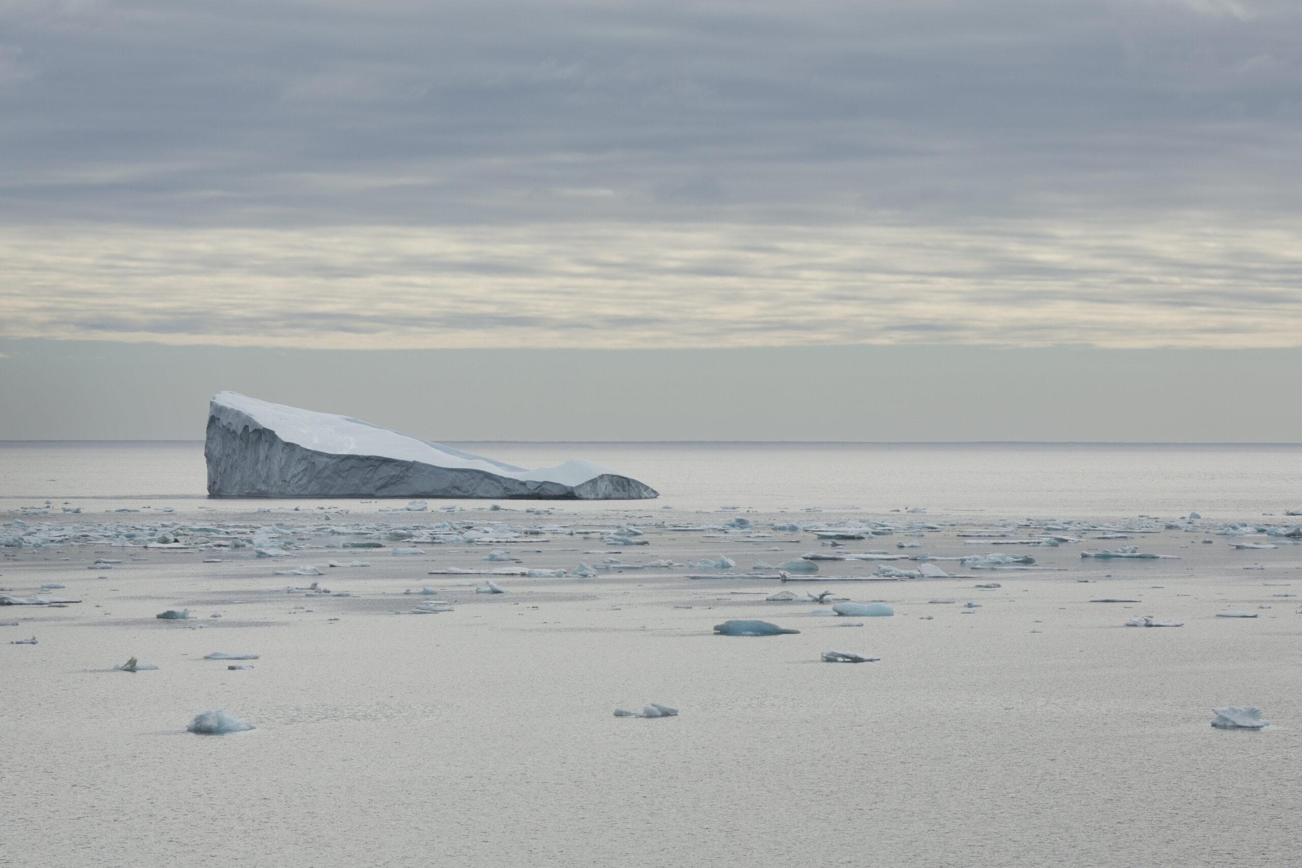 Ein Eisberg auf der linken Seite des Bildes, rundherum schwimmen kleine Einsstücke im Wasser