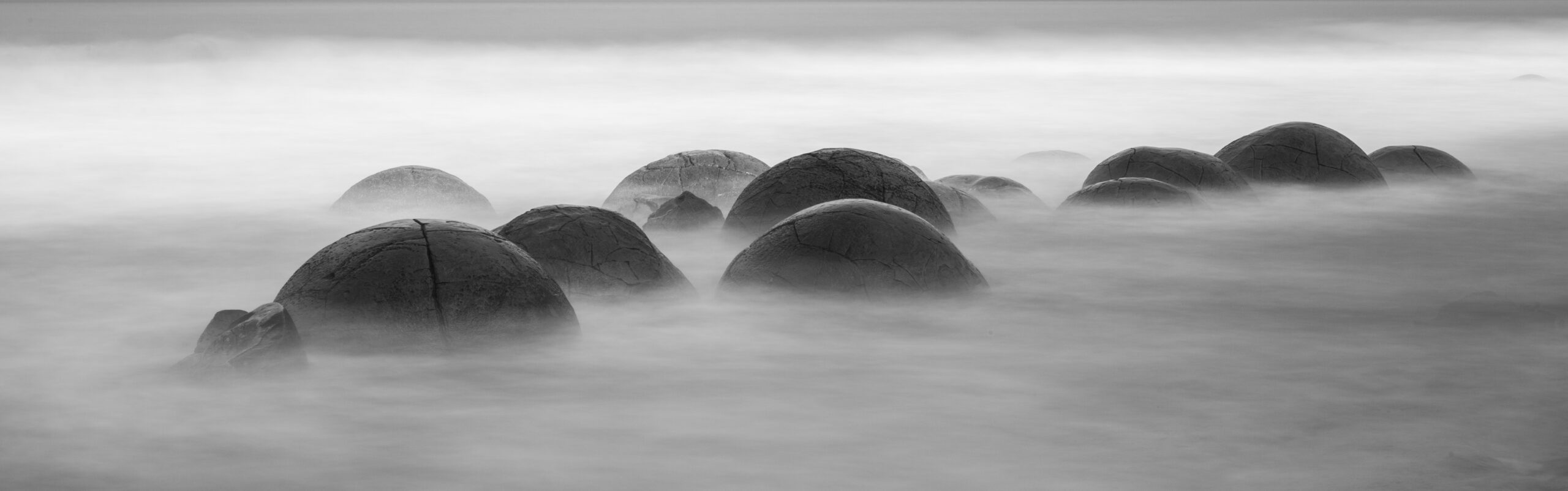 Die Moeraki Boulders in Neuseeland bei Langzeitbelichtung zur Hälfte im Wasser in Schwarz und Weiß