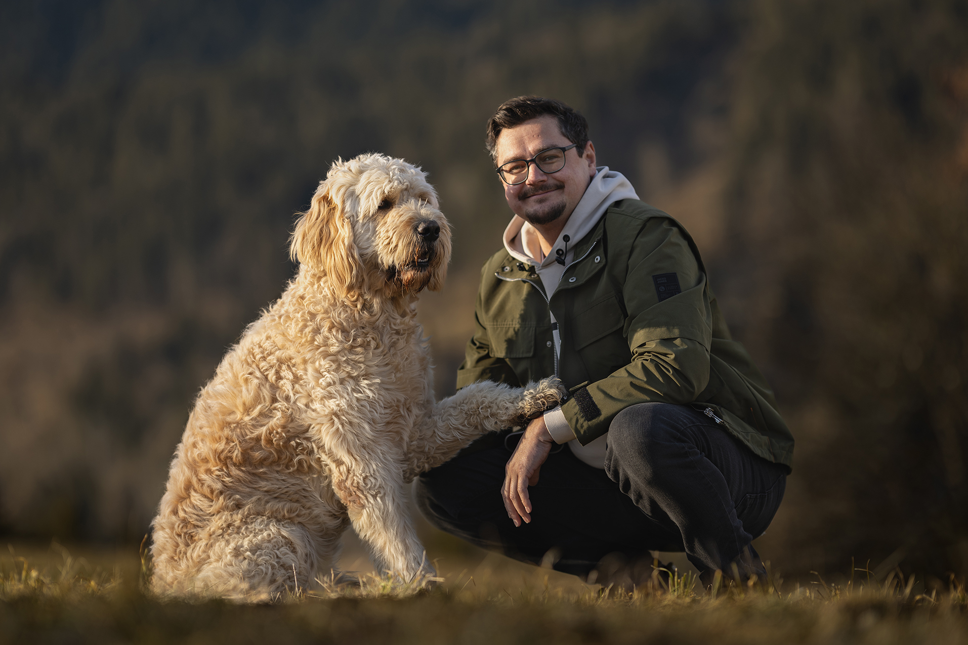 Junger Mann mit einem Golden Doodle, der seine Pfote am Arm des Mannes hat.