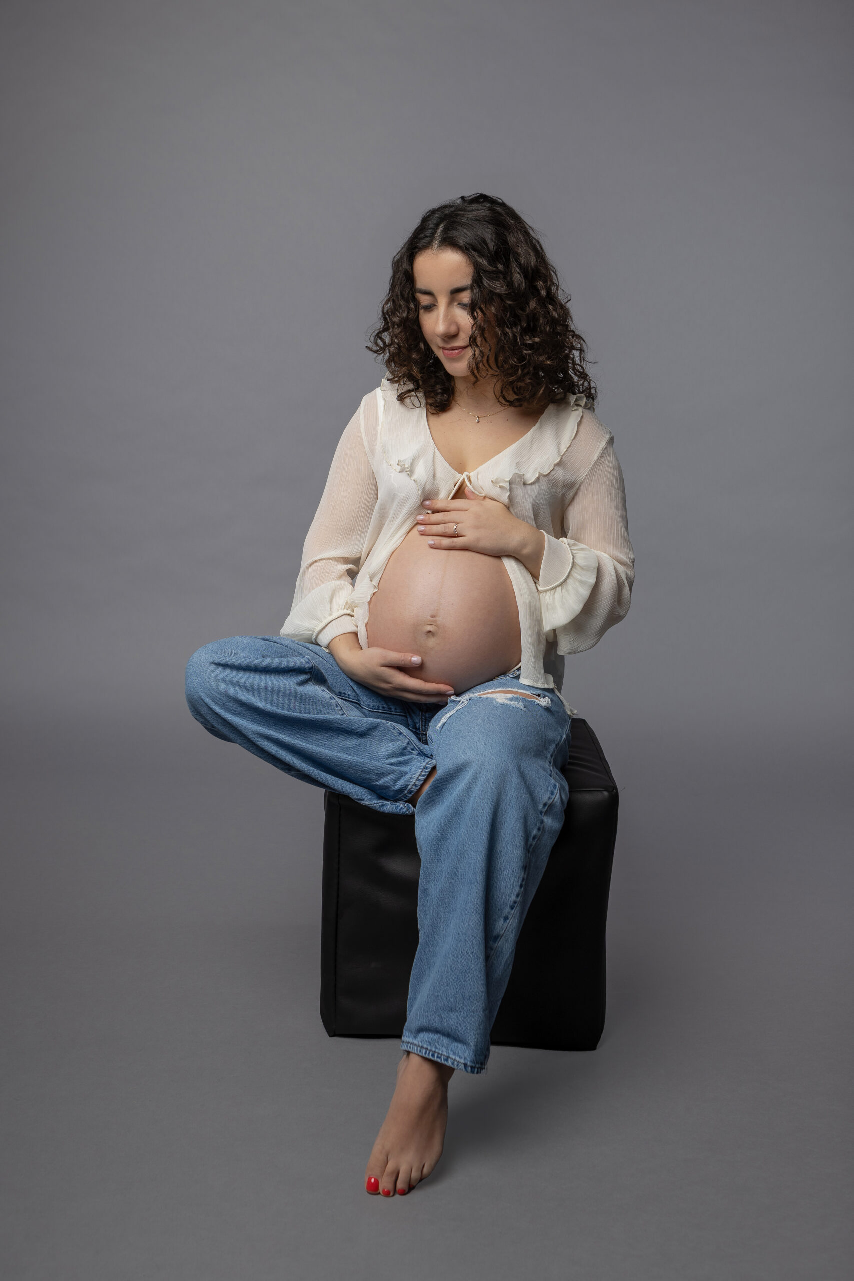 Junge schwangere Frau sitz auf einem schwarzen Würfel vor grauem Hintergrund