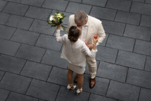 Hochzeitspaar in weiß von oben fotografiert, umgeben von dunklen Betonfliesen