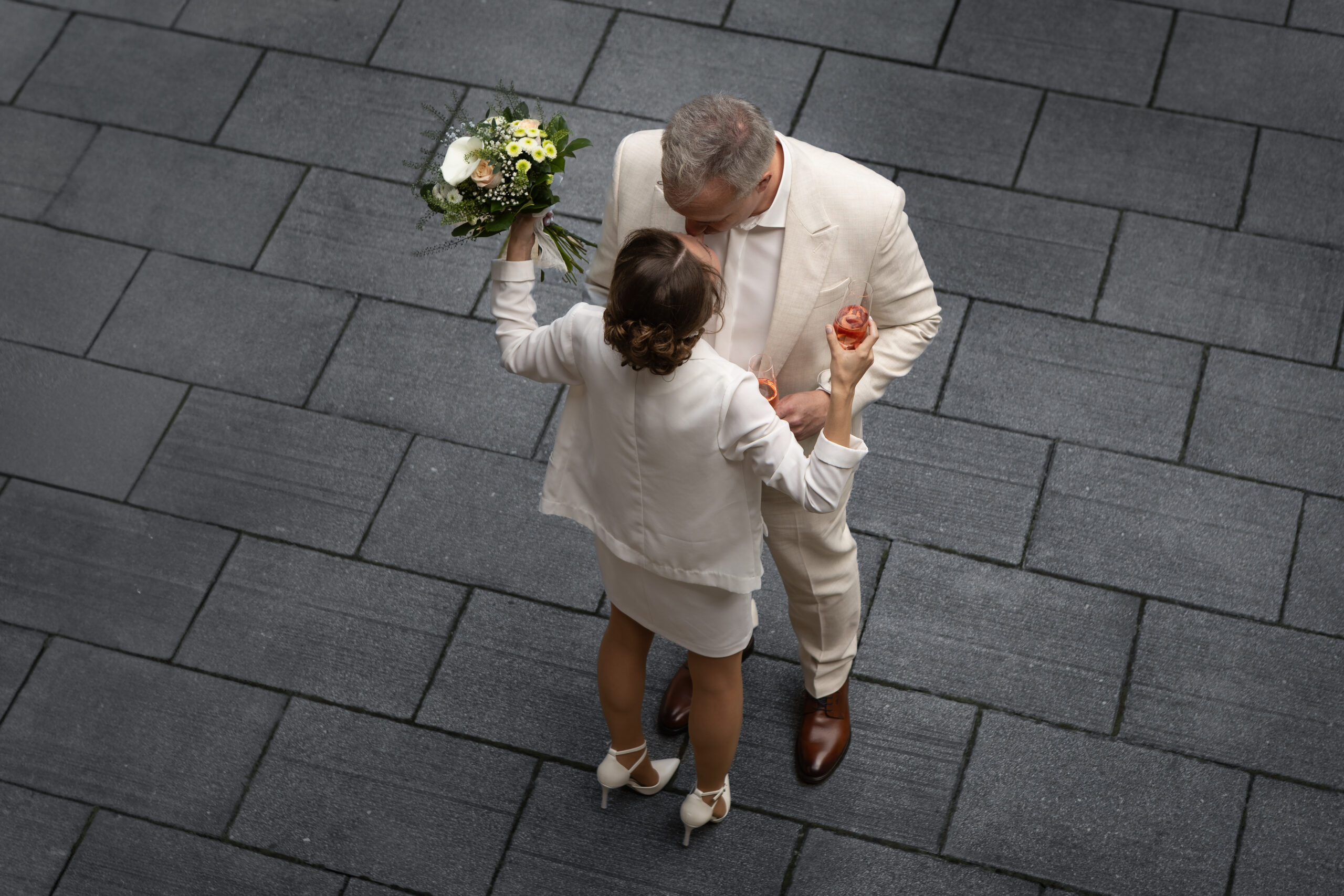 Hochzeitspaar in weiß von oben fotografiert, umgeben von dunklen Betonfliesen