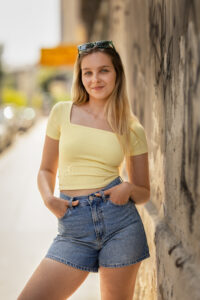 Blonde junge Frau steht an der Wand auf der Straße und blickt in die Kamera