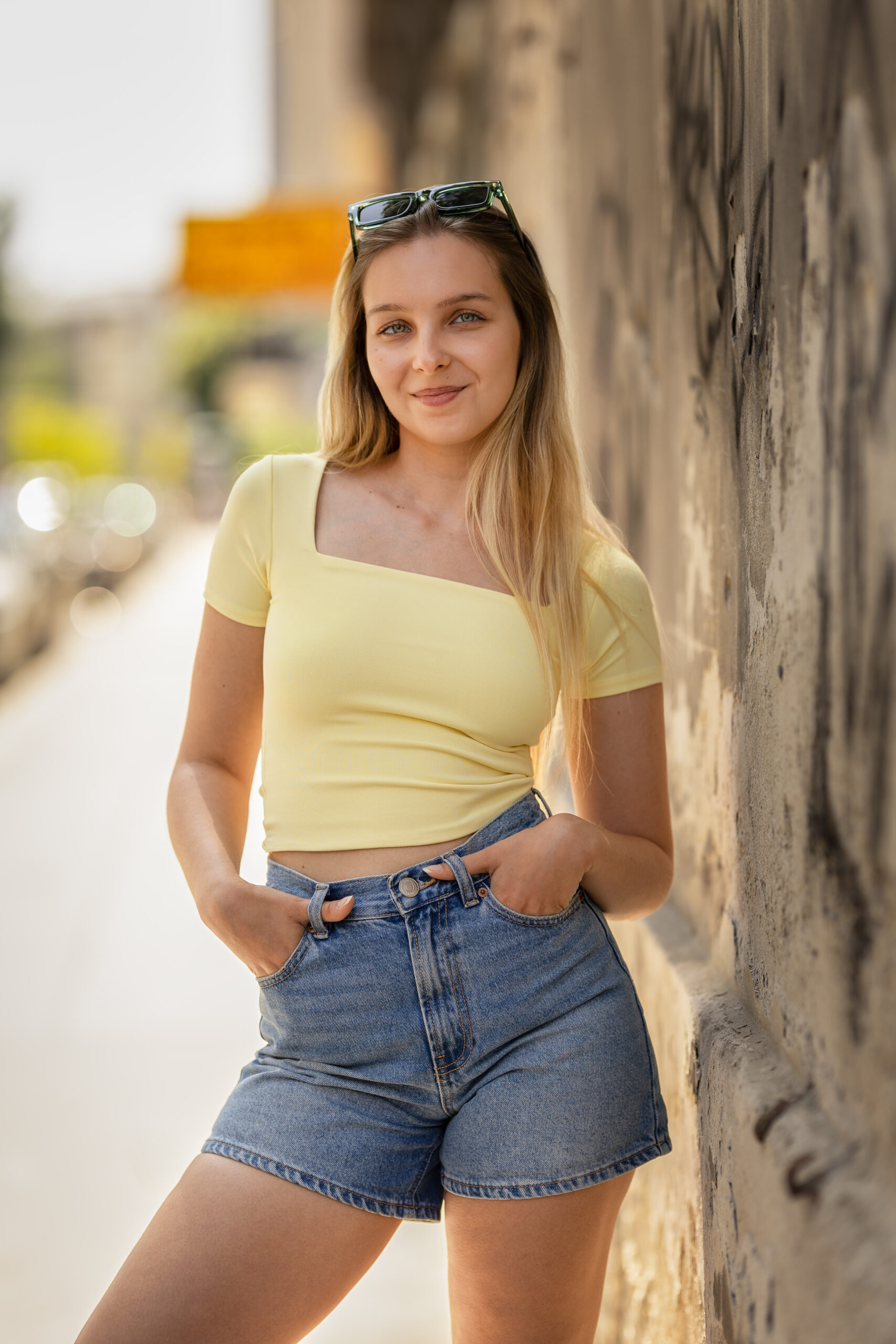 Blonde junge Frau steht an der Wand auf der Straße und blickt in die Kamera