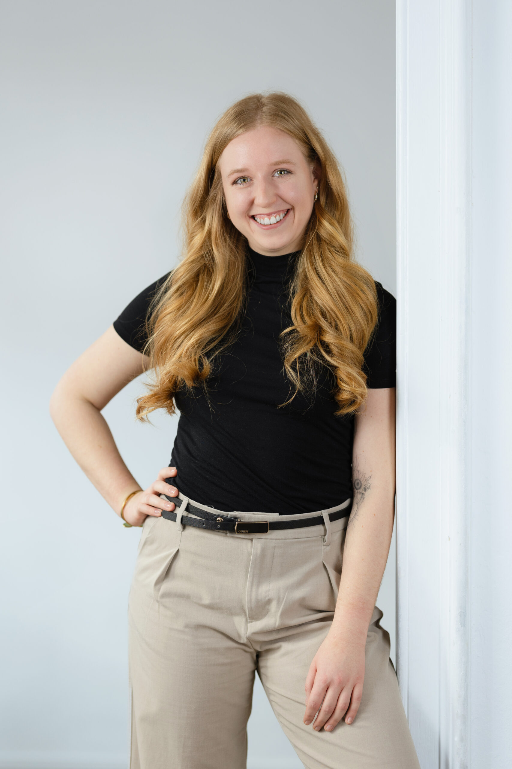Junge rothaarige Frau mit schwarzem Shirt steht angelehnt an die Wand und lächelt in die Kamera
