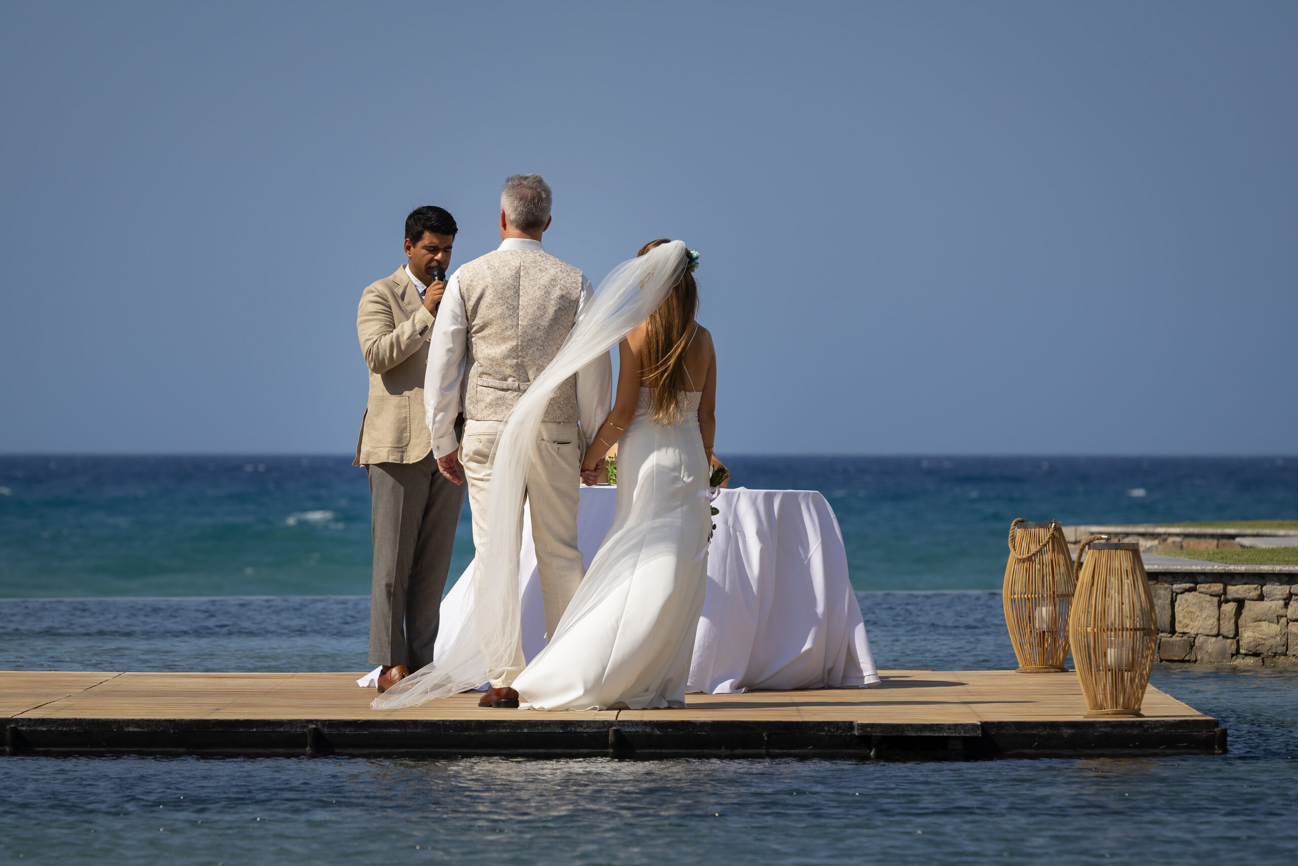 Hochzeitspaar steht während der Trauung auf einem Steg im Wasser, hinter ihnen das Meer